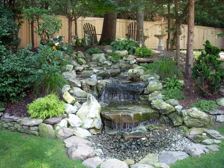 Rock waterfall in a landscaped garden with trees and plants